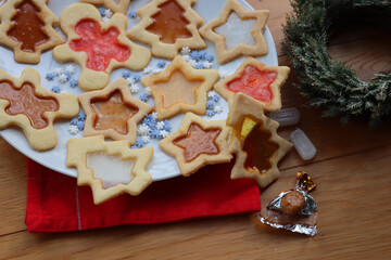 Christmas cookies with fake “glass” made of melted candies on plate on wooden table with festive decorations