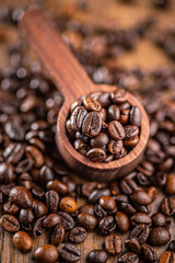 Roasted coffee beans in wooden scoop on wooden table.