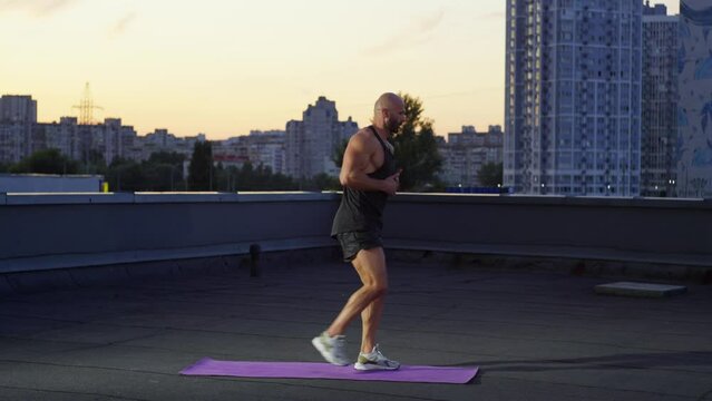 Handsome muscular athlete doing fitness at sunset in cityscape. Active, healthy and sweaty lifestyle of the boy. High quality 4k footage