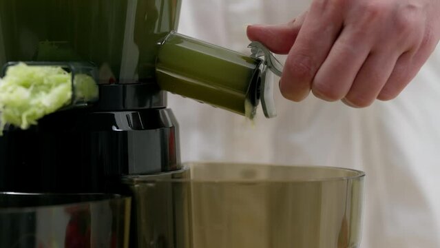 A woman drains vegetable juice from a juicer. Healthy detox vegetarian diet with cold pressed plant extractor for bread and smoothies.