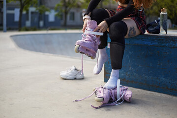 Female roller blader puts on aggressive in-line skates in a skatepark