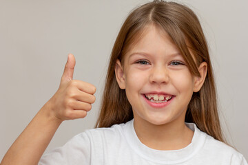 Portrait of caucasian happy little girl with open wide smile holding thumb up looking at camera