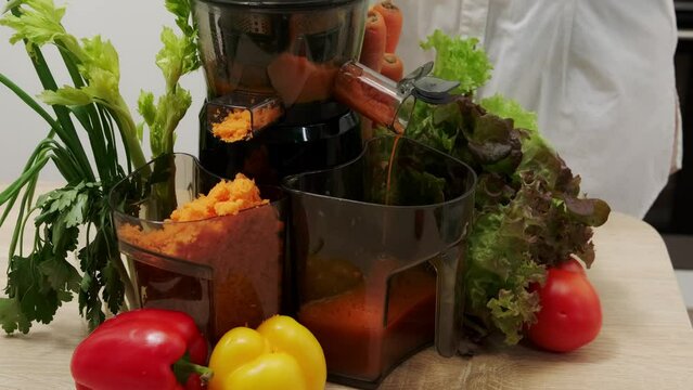 A woman makes vegetable juice using a juicer in her home kitchen. Healthy detox vegetarian diet with cold pressed plant extractor to extract nutrients for smoothies.