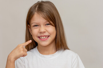 Portrait of caucasian little girl with open wide smile showing on good teeth by index finger looking at camera