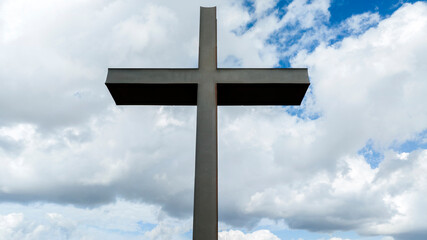 Closeup of a metal sculpture of a Christian cross. In the background the blue sky with some clouds creates a mystical atmosphere.