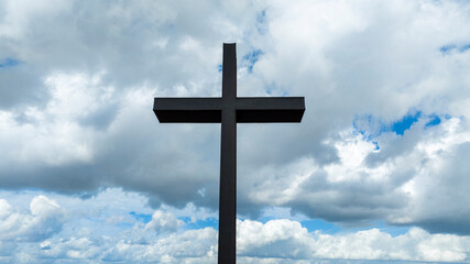 Closeup of a metal sculpture of a Christian cross. In the background the blue sky with some clouds creates a mystical atmosphere.