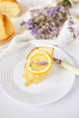 Piece of lemon cake on white table with lavender flower bouquet