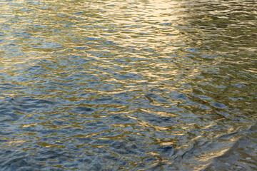 abstract reflecions of sunlight on the rippled water surface in the morning golden and gray background