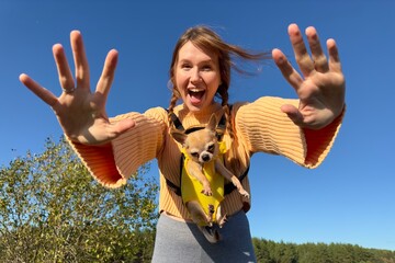Happy young woman or teenager girl walking with her puppy Chihuahua dog in the forest or park at...