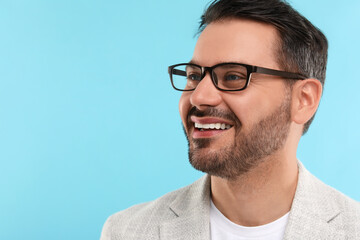 Obraz premium Portrait of happy man in stylish glasses on light blue background, space for text