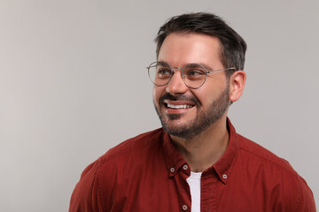 Obraz premium Portrait of happy man in stylish glasses on light grey background. Space for text