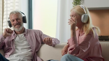 Joyful senior elderly Caucasian married couple grandparents man woman listening music using headphones dancing fooling around having fun carefree grandmother grandfather enjoying weekend at home couch - Powered by Adobe