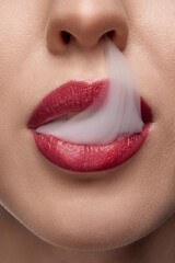 Cropped photo. Extreme close up of woman with red lips blowing smoke from mouth. Bad habits. No smoking or quit smoking.