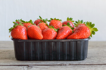 Ripe strawberries in a black box on a wooden table. High quality photo