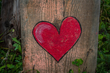 Un cuore rosso dipinto su un tronco di legno di una staccionata