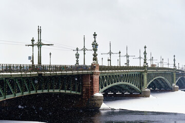 An ancient beautiful bridge over the river in winter. It's snowing outside.