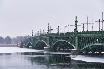 An ancient beautiful bridge over the river in winter. It's snowing over the city.