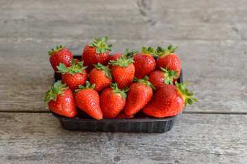 Ripe strawberries in a black box on a wooden table. High quality photo