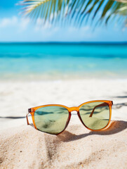 Fototapeta na wymiar Closeup of black protective sunglasses on sandy beach at tropical seaside on warm sunny day.