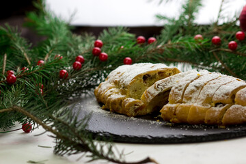 The stolen is cut into slices. Classic German cupcake on a black plate. Plate surrounded by Christmas tree branches