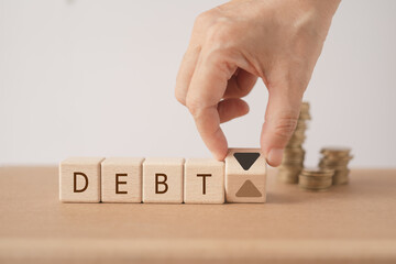 DEBT word on wooden cube blocks word with hand flipped up to down arrow and blurred stack of coin  for Financial debt decrease, revenue management  concept - obrazy, fototapety, plakaty