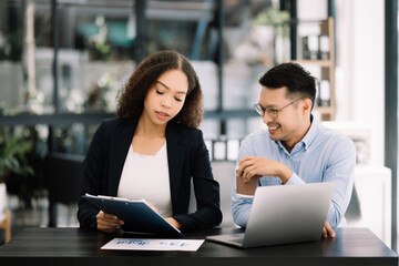 Two Asian businesswoman and man discuss investment projec with tablet laptop computer.