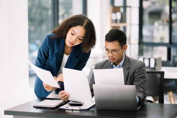 Two Asian businesswoman and man discuss investment projec with tablet laptop computer.