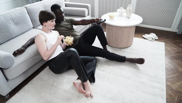 Young afroamerican man and caucasian woman watching TV, aeting chips