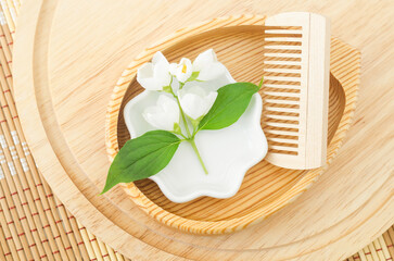 Small wooden plate with wooden hairbrush (comb) and jasmine flowers. Natural hair care, homemade spa and beauty treatment recipe.