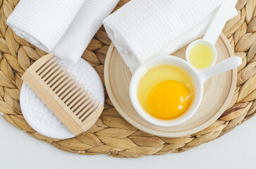 Small white bowl with raw egg and wooden hairbrush. Natural skin and hair care, homemade spa and beauty treatment recipe. Top view