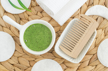 Homemade green tea (kelp, algae, spirulina) face or hair mask (scrub) in a small white bowl and wooden hairbrush. Natural beauty treatment and spa recipe. Top view.
