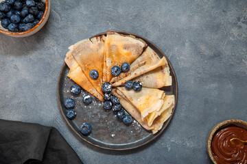 Thin pancakes with chocolate spread and blueberries on the grey background top view