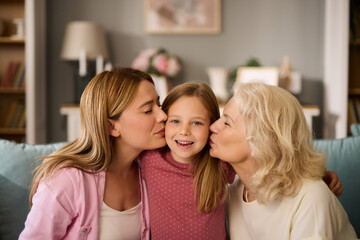 Mother and grandmother kissing little girl at home