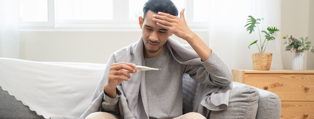 Seasonal cold sickness in people concept, Sick asian man looking at thermometer during measuring...
