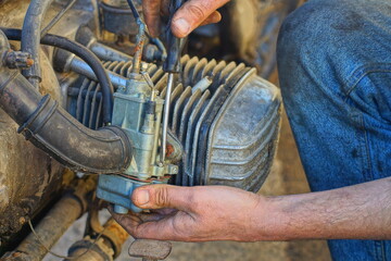 worker with his hands removes a dirty old industrial iron retro carburetor from an iron engine while repairing a retro classic heavy motorcycle on the street during the day