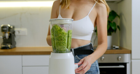 Woman is making green spinach and banana smoothie in blender. 