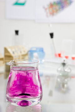Close up of a glass container filled with  fluid and dark pink chemical solution
