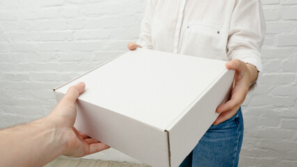 Young woman receiving parcel from delivery man, white brick background.