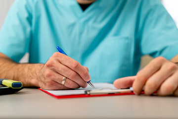 Close-up shot of a male doctor's hand with ring on his finger filling out a patient's medical...
