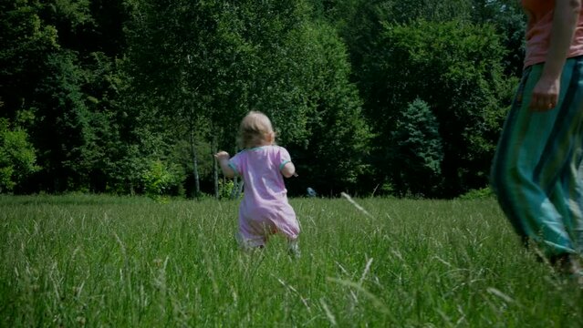 The baby learns to take the first steps. A cute little girl is learning to walk on a blade of grass. The baby laughs happily. A happy family.