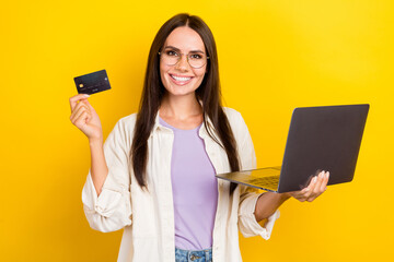 Photo portrait of attractive young woman hold netbook credit card dressed stylish white clothes isolated on yellow color background