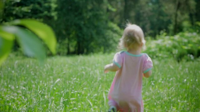 The baby learns to take the first steps. A cute little girl is learning to walk on a blade of grass. The baby laughs happily. A happy family.