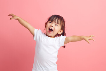 Joyful little Asian girl with her arms outstretched expresses fun and pleasure on isolated pink...
