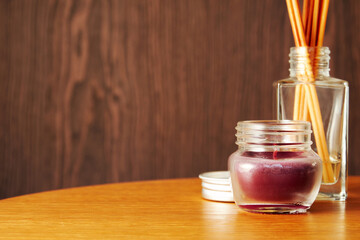 Red perfume candle on the wooden table with scented wooden sticks. Cozy home interior backgrounds....