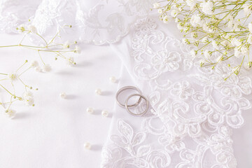 Two white gold wedding rings lie on the bride's white patterned gloves among beads of pearls...