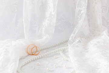 Delicate waves of a wedding veil or tulle with two wedding rings on it. wedding pearl beads of the bride. Front view. A copy of the space.