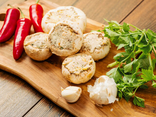 Stuffed mushrooms cups and chilly peppers and garlic cloves on a wooden board and table. High quality product with breadcrumbs, cheese and herbs ready for oven cooking.