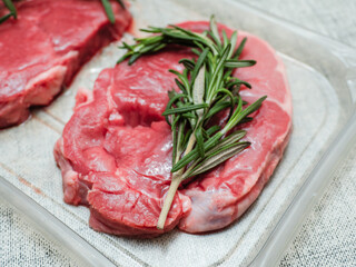 Juicy uncooked lamb leg steak with green fresh rosemary on plastic tray. Uncooked high quality meat product with rich taste and vivid color.
