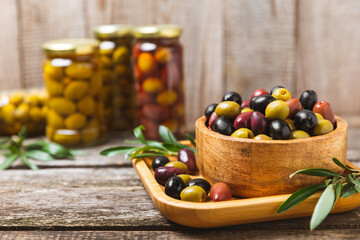 Green, black and red olives, olive oil on a brown wooden background. Fresh juicy olives in a bowl and fresh olive leaves. Vegan. Olive fruits. Place for text. Copy space.