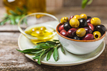 Green, black and red olives, olive oil on a brown wooden background. Fresh juicy olives in a bowl and fresh olive leaves. Vegan. Olive fruits. Place for text. Copy space.